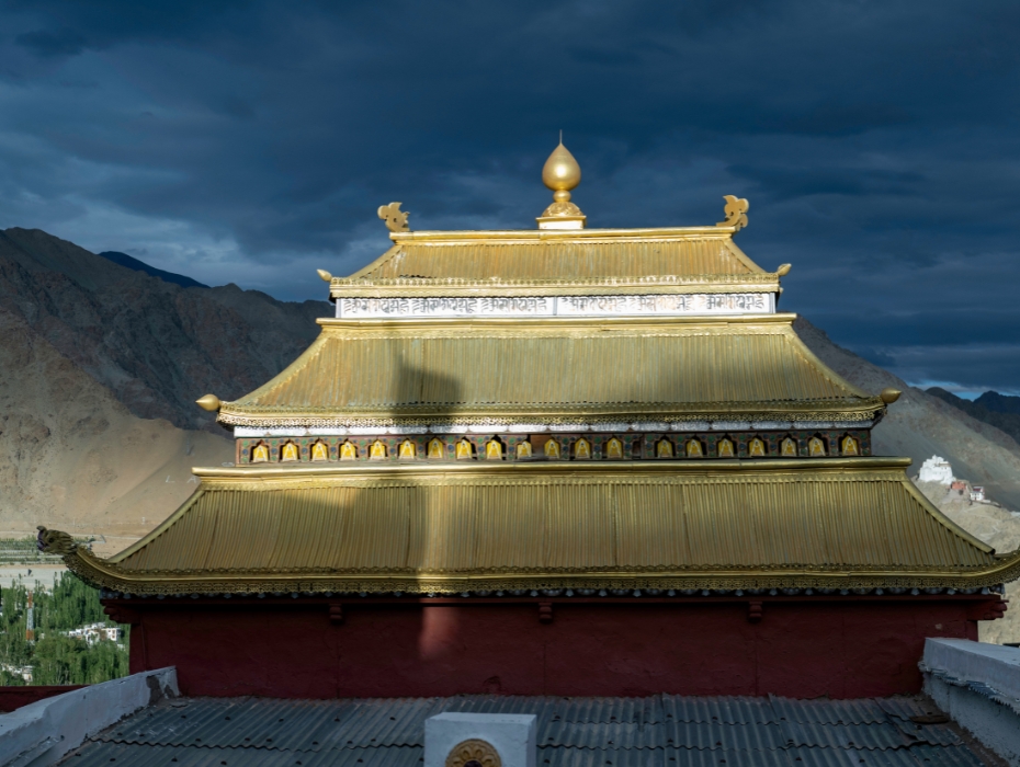 Ornate golden-roofed Buddhist monastery with traditional Tibetan architecture against dramatic Ladakh mountain backdrop