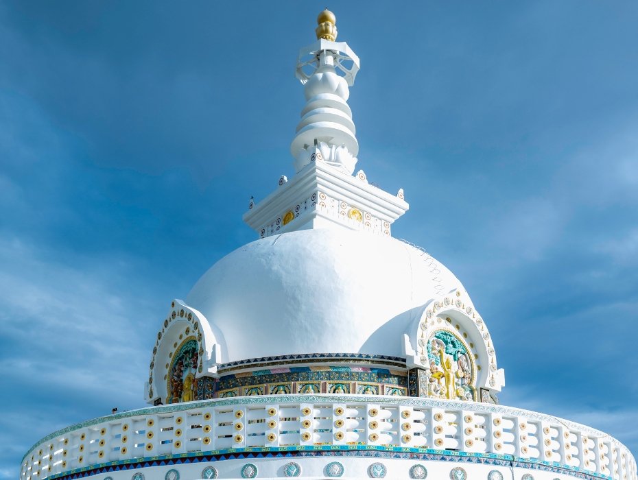 Ornate white Buddhist stupa with golden decorations and prayer wheels in Ladakh against blue sky