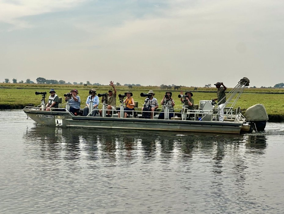 Photography safari boat with guests and cameras on Chobe River, Botswana, elephants visible in background